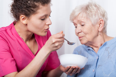 Nurse aid assisting elderly woman for her meal