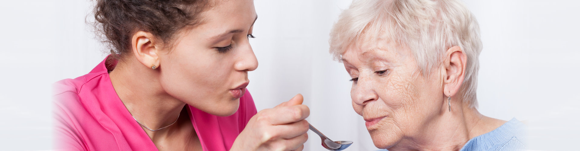 Nurse aid assisting elderly woman for her meal